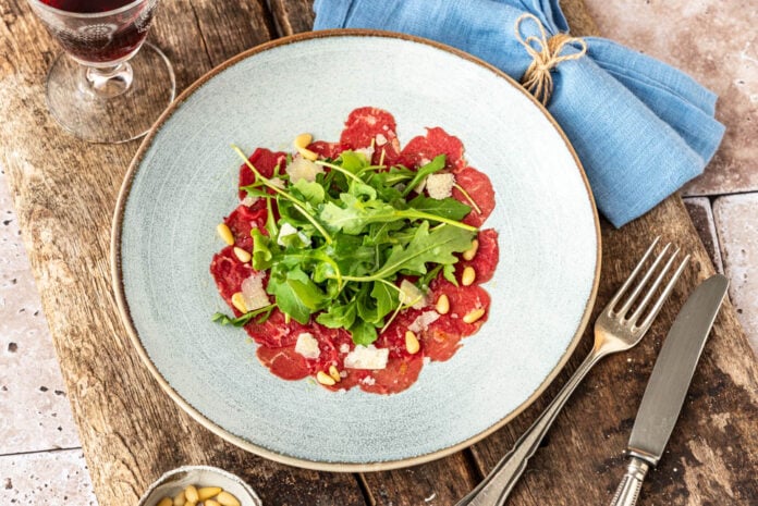 Klassisches Carpaccio auf Holzuntergrund mit Besteck