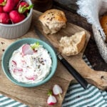 Brotaufstrich mit Radieschen und Brötchen auf Brett