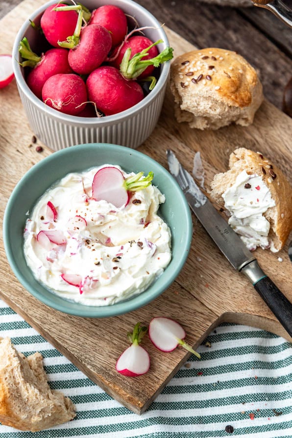 Brotaufstrich mit Radieschen und Brötchen auf Brett