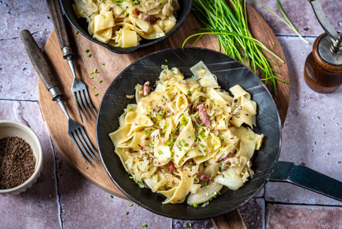 Zwei Pfannen mit Krautfleckerl auf einem Brett mit Schnittlauch