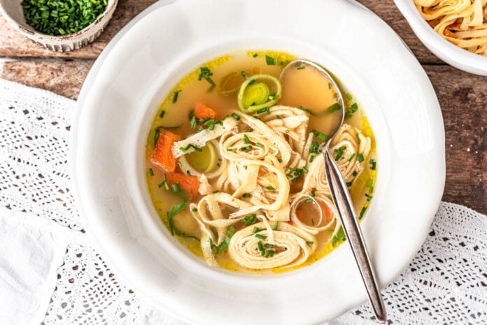 Flädlelsuppe in einem Suppenteller mit Löffel und Schnittlauch