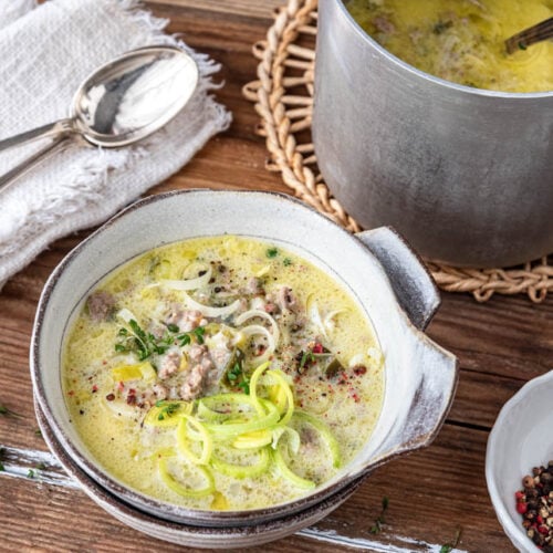 Eine Schüssel mit Käse-Lauch-Suppe. Daneben der Kochtopf.