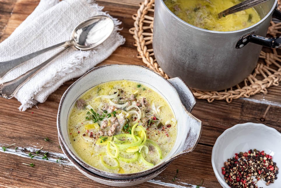 Eine Schüssel mit Käse-Lauch-Suppe. Daneben der Kochtopf.