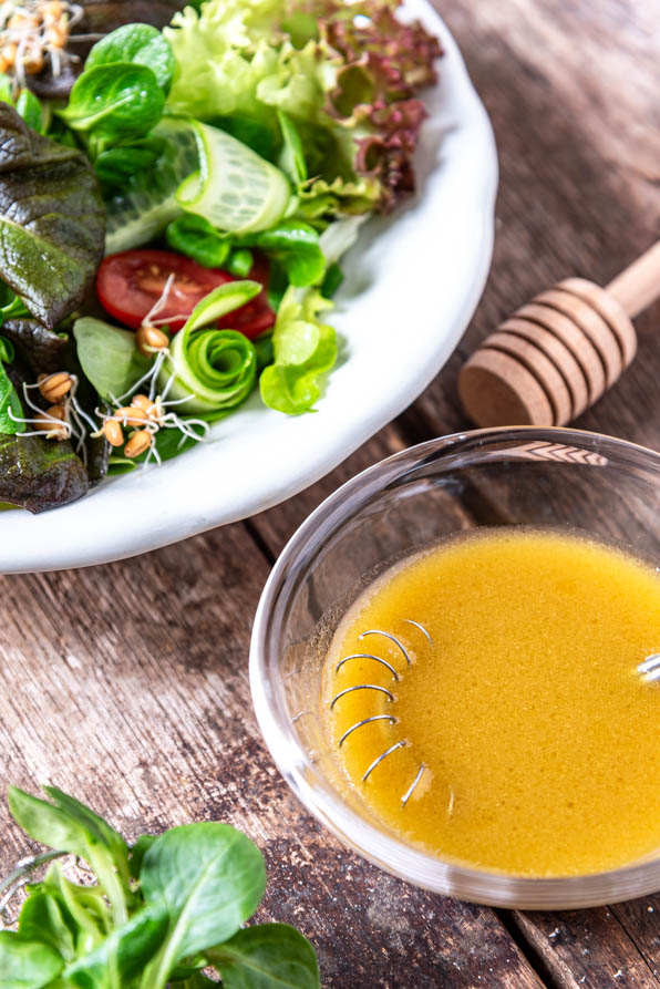 Honig-Senf-Dressing in Schüsselchen neben Salatteller