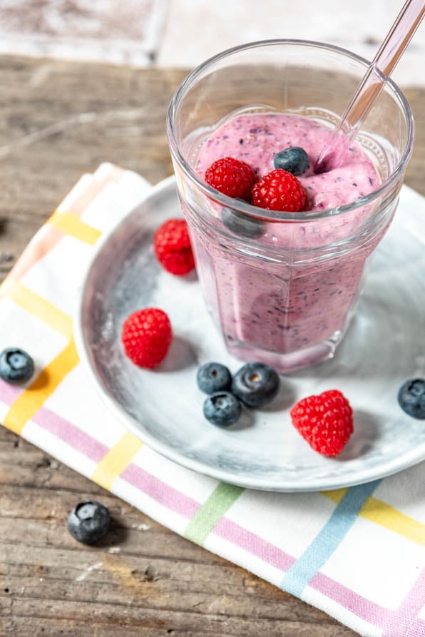 Beeren Smoothie in einem Glas mit Strohhalm und Beeren drumherum