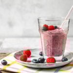 Beeren Smoothie in einem Glas mit Strohhalm und Beeren drumherum