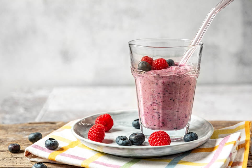 Beeren Smoothie in einem Glas mit Strohhalm und Beeren drumherum