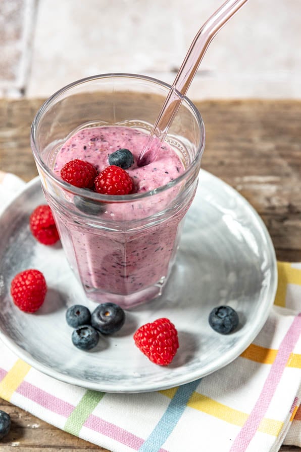 Beeren Smoothie in einem Glas mit Strohhalm und Beeren drumherum