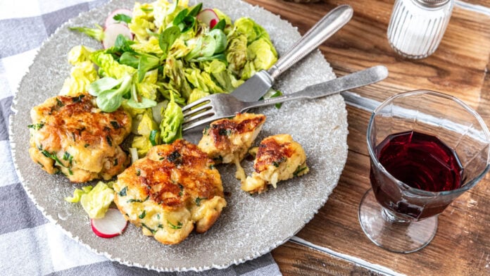 Kaspressknödel mit Salat und einem Glas Wein auf Holztisch - Foodblog Mundgefühl