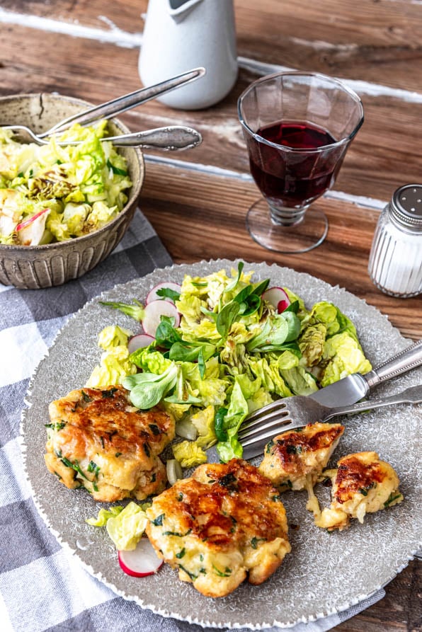 Kaspressknödel mit Salat und einem Glas Wein auf Holztisch