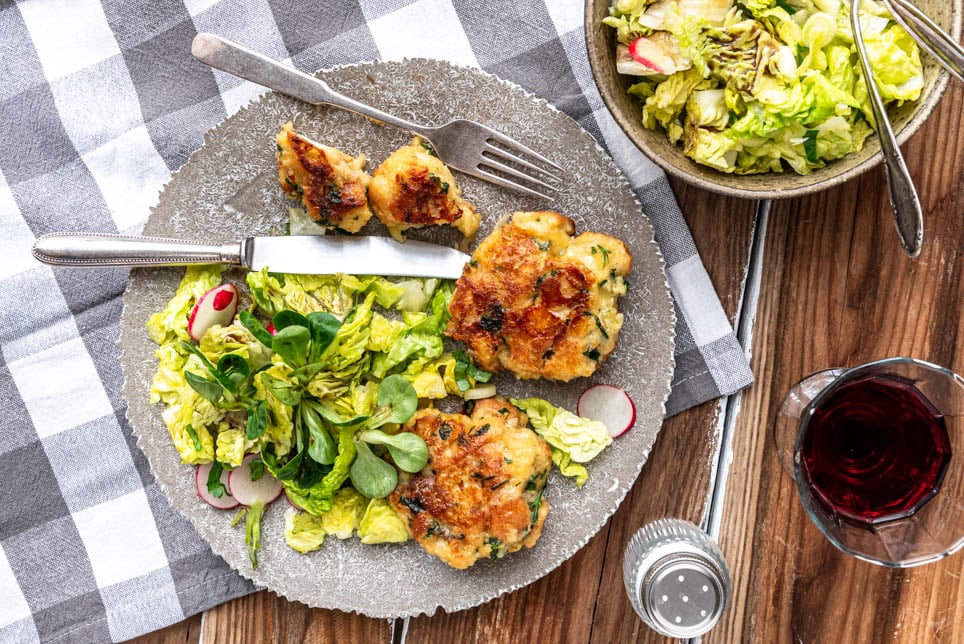 Kaspressknödel mit Salat und einem Glas Wein auf Holztisch