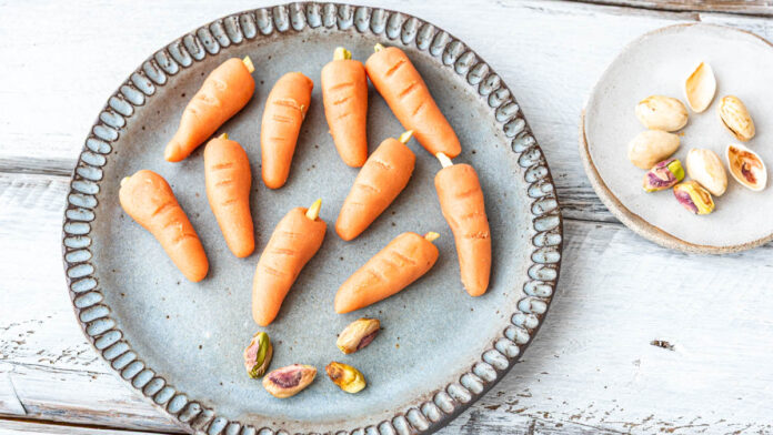marzipan-moehren-selber-machen3 Marzipan-Möhren auf einem Teller. Daneben Pistazien - Foodblog Mundgefühl