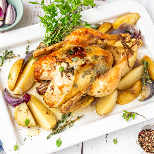 Ganzes Hähnchen im Backofen mit Kartoffeln auf Servierplatte und Holzuntergrund