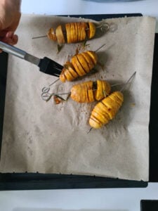 Die eingeschnittenen Kartoffeln auf Spießen werden mit Marinade bestrichen