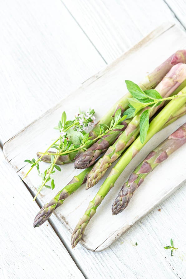 grüner Spargel auf Holzbrett mit Kräutern