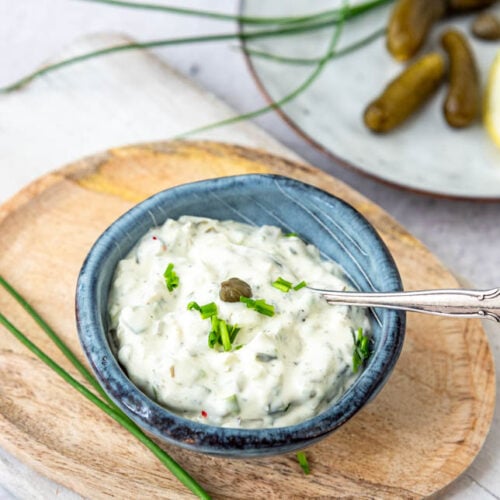 Schälchen mit Sauce Tartare auf Holzteller und Cornichons