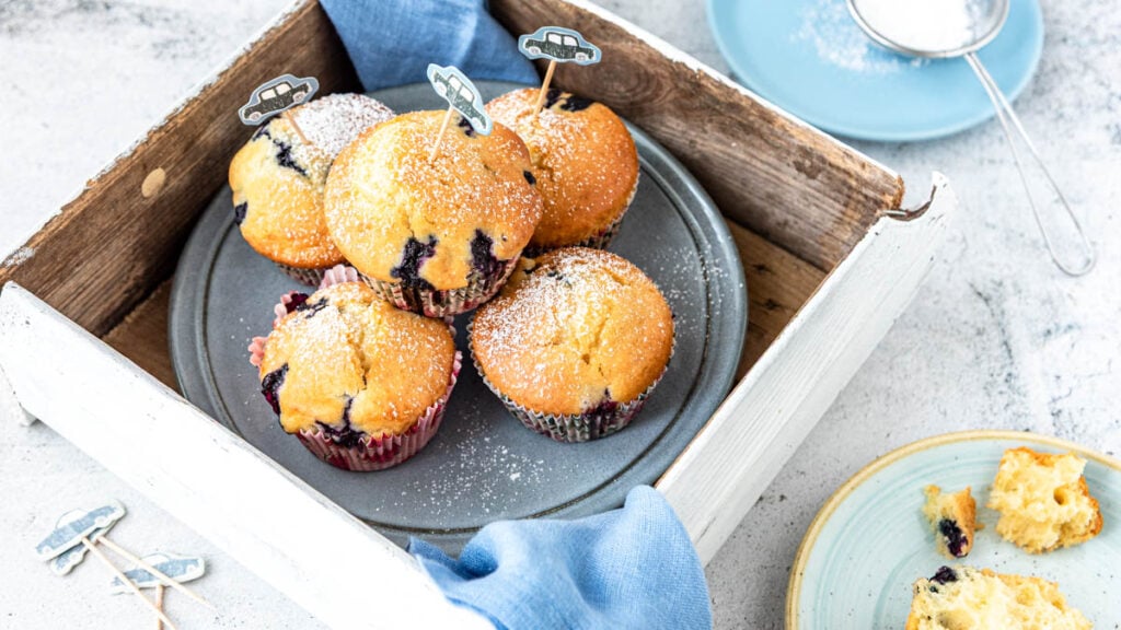 Blaubeermuffins auf Teller in Holzbox mit kindlicher Deko