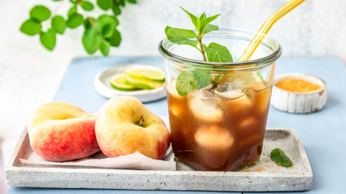 eistee-selber-machen Glas mit selbstgemachtem Pfirsich Eistee, Pfirsichen und Eiswürfeln