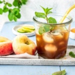 Glas mit selbstgemachtem Pfirsich Eistee, Pfirsichen und Eiswürfeln auf einem Tablett