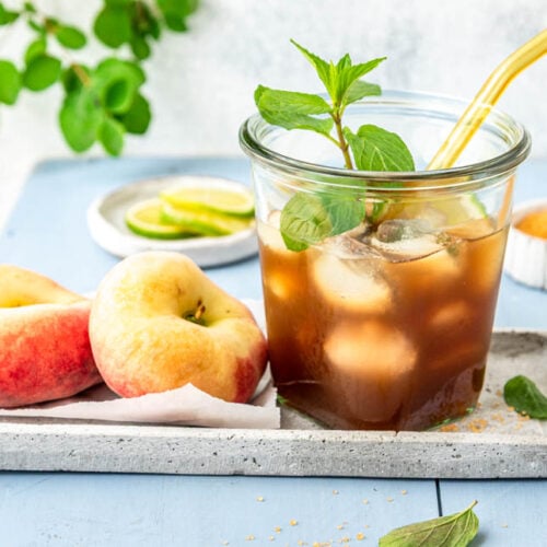 Glas mit selbstgemachtem Pfirsich Eistee, Pfirsichen und Eiswürfeln auf einem Tablett
