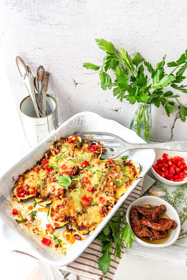 gefüllte Zucchini vegetarisch ohne Kohlenhydrate in Auflaufform. Daneben Gemüse und Besteck