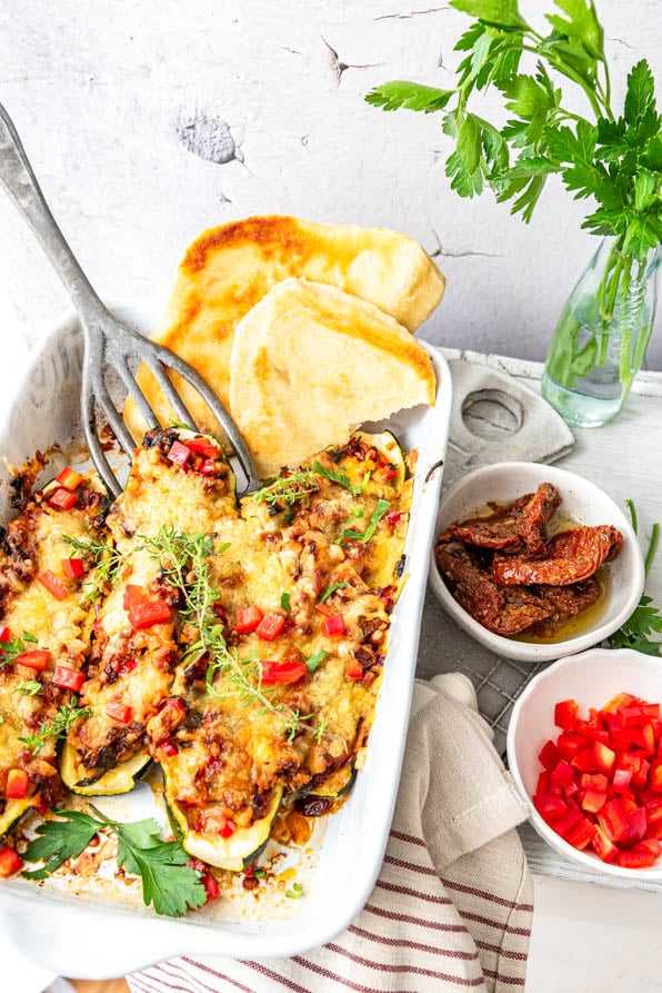 gefüllte Zucchini vegetarisch low carb in Auflaufform. Daneben Fladenbrot