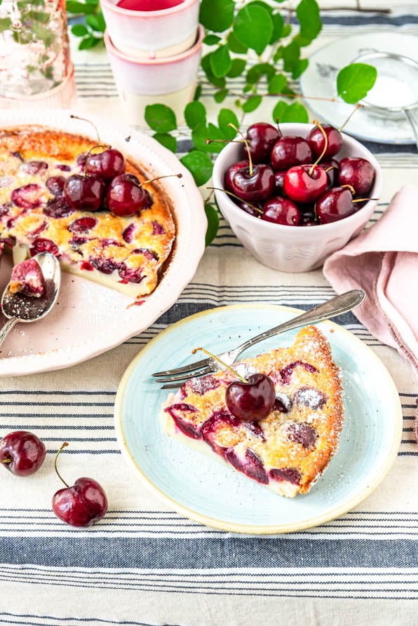 Ein Stück französischer Clafoutis auf Teller neben Auflaufform