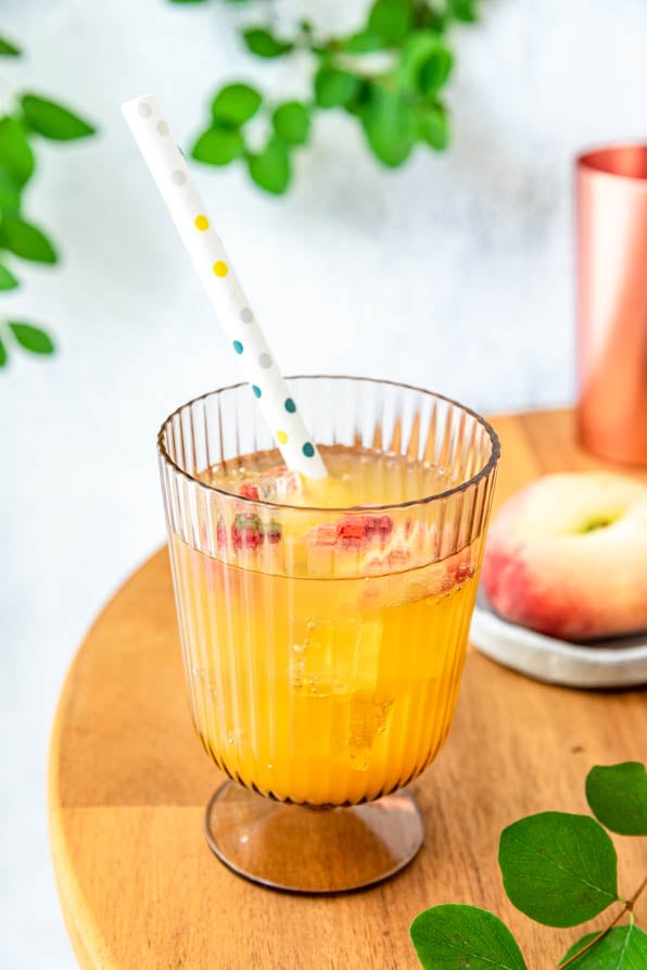 Der Sommerdrink Peach Perfect Spritz im Glas mit Strohhalm und Pfirsichen