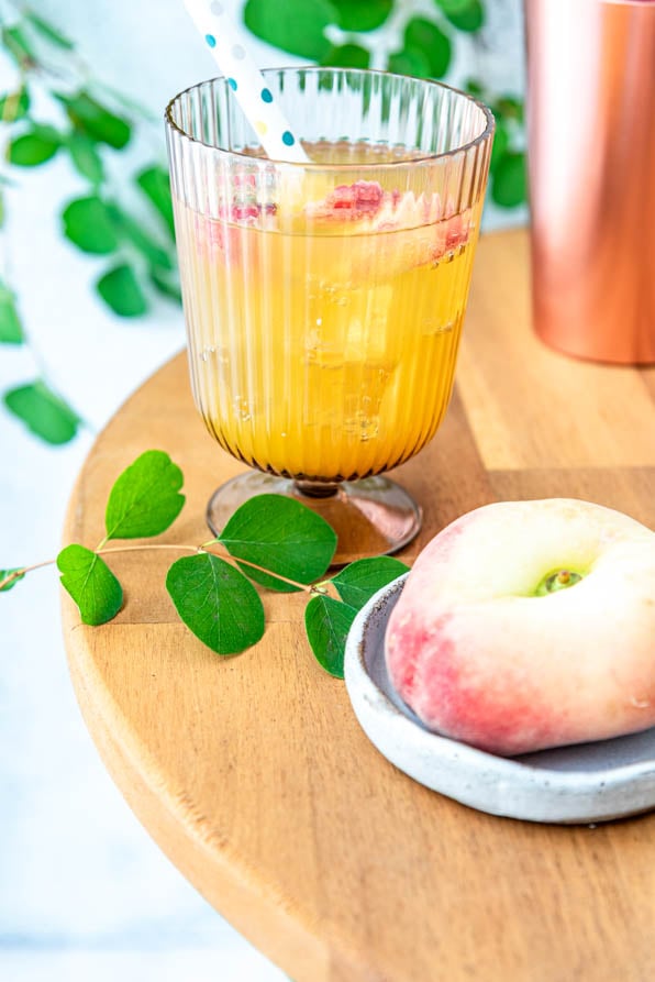 Ein Glas Peach Perfect Spritz auf einem Tisch mit einer Pfirsich daneben