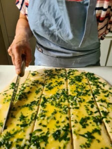 Mit Kräuterbutter bestrichener Hefeteig wird in Spalten geschnitten für Zupfbrot Rezept