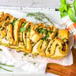 Frisch gebackenes Zupfbrot auf Backpapier und daneben Kräuter