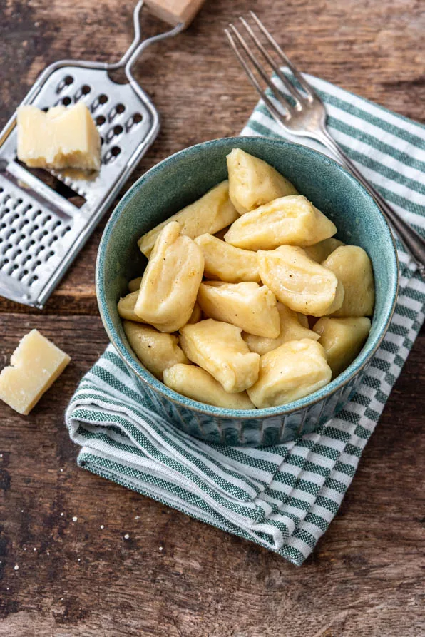 hausgemachte Gnocchi in Schüssel, daneben Parmesan mit Hobel
