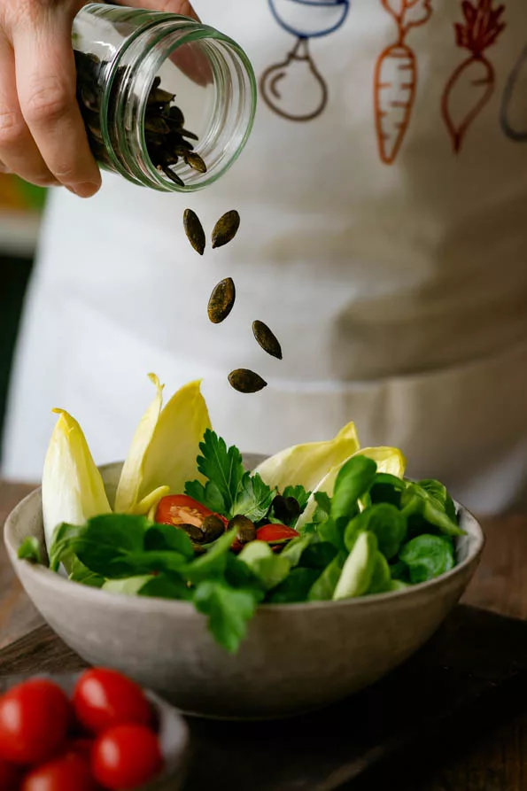Geröstete Kürbiskerne werden aus einem Glas auf den Salat gekippt