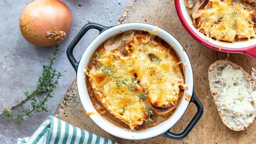Französische Zwiebelsuppe in einer weißen ofenfesten Schale mit goldbraun überbackenem Baguette und Thymian.