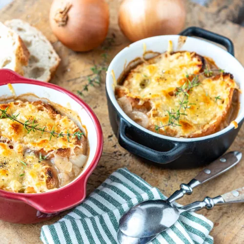 Goldbraun überbackene Französische Zwiebelsuppe mit Baguettescheiben und Kräutern in einer zwei kleinen Gratinformen serviert