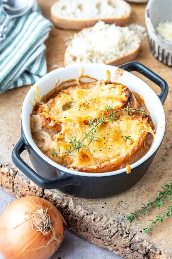 Französische Zwiebelsuppe mit Käsekruste, daneben Zwiebel und Baguette