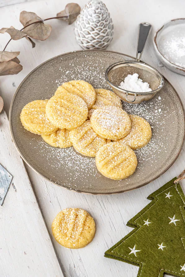 Weihnachtsplätzchen aus Puddingpulver auf Teller mit grünem Tannenbaum
