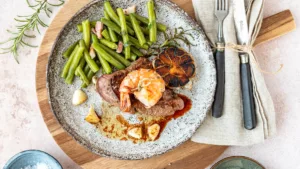 Surf and Turf mit saftigem Rindersteak und gebratener Garnele, serviert mit grünen Bohnen