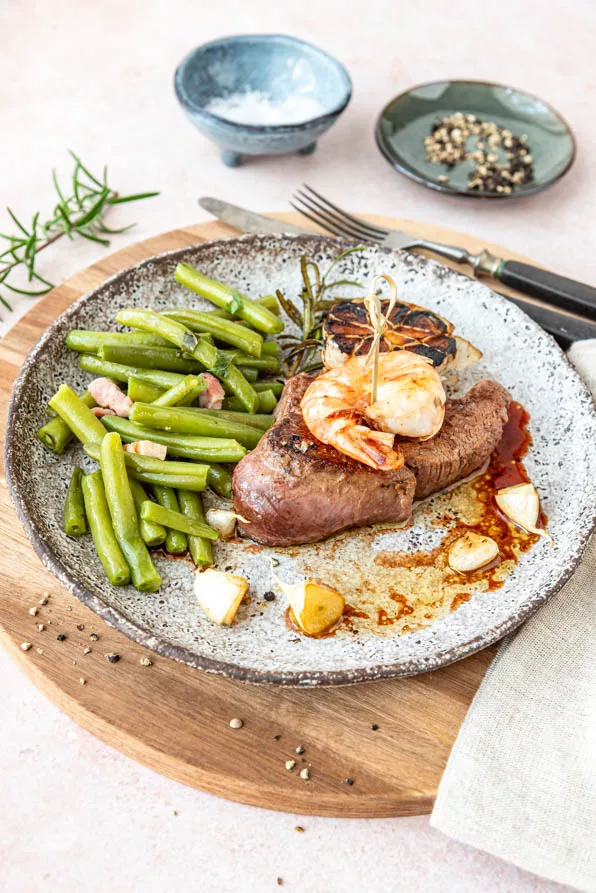 Saftiges Steak mit gebratener Garnele und grünen Bohnen auf einem Keramikteller
