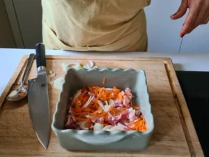 In die Ofenform kommen geraspelte Karotten, Speck und Zwiebelringe