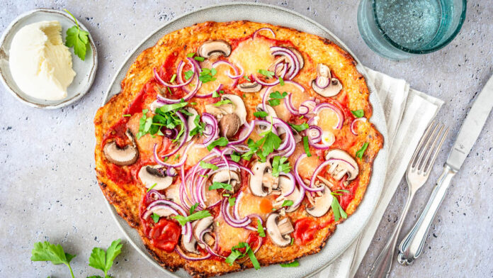 blumenkohlpizza Blumenkohlpizza mit knusprigem Boden, Tomatensauce, Mozzarella, Champignons und roten Zwiebeln auf hellem Teller