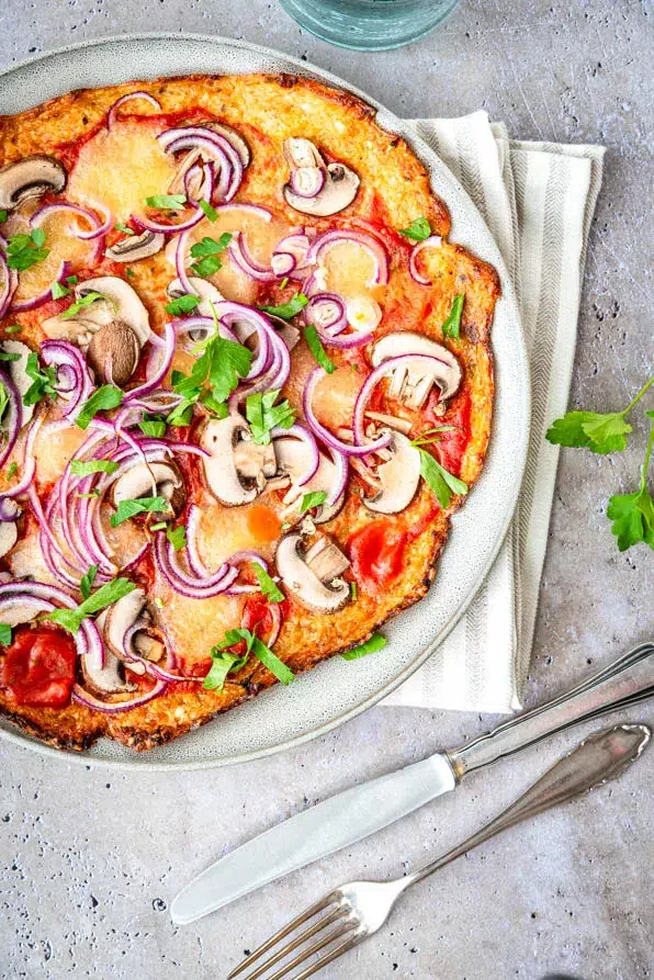 Draufsicht auf eine selbstgemachte Blumenkohlpizza mit Champignons, roten Zwiebeln und Mozzarella auf grauem Teller