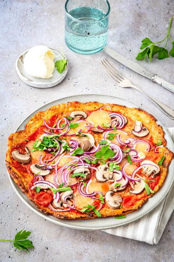 Knusprige Blumenkohlpizza frisch gebacken, bunt belegt mit Gemüse und Kräutern, serviert auf einem hellen Tisch