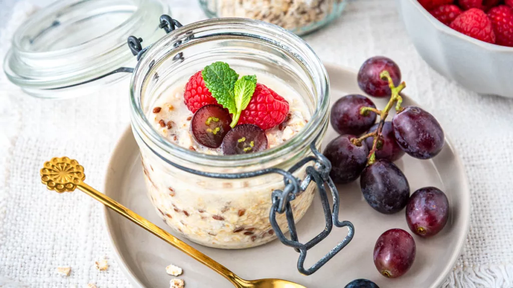 Overnight Oats im Glas mit Himbeeren, Weintrauben und Minze als gesundes Frühstück