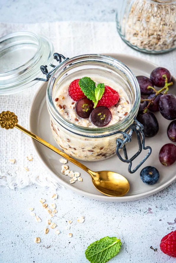 Overnight Oats Rezept im Glas mit Haferflocken, Milch, Himbeeren und Trauben dekoriert