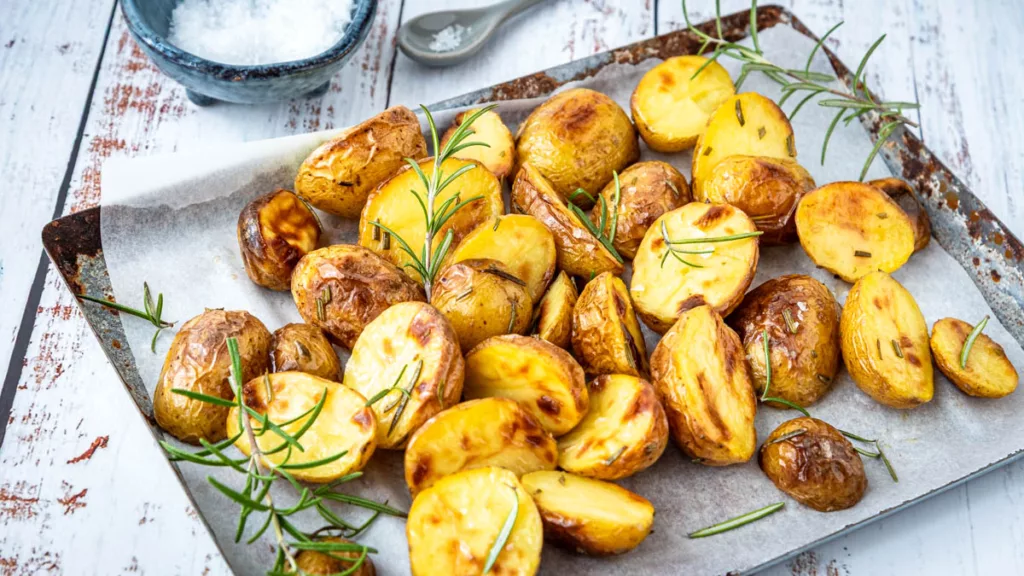 Rosmarinkartoffeln aus dem Ofen goldbraun gebacken auf einem Blech mit frischem Rosmarin und grobem Salz