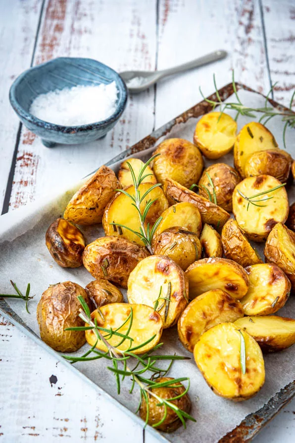 Knusprige Rosmarinkartoffeln aus dem Ofen mit krossen Schnittflächen und aromatischen Rosmarinzweigen auf Backpapier