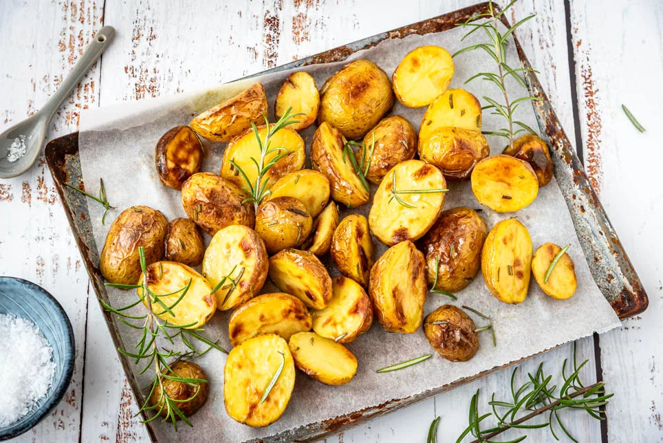 Goldbraune Kartoffelhälften mit Rosmarin direkt vom Blech serviert, einfache und aromatische Beilage aus dem Ofen
