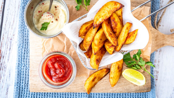 kartoffelecken3 Kartoffelecken aus dem Ofen knusprig gebacken mit Ketchup und Dip auf Holzbrett serviert