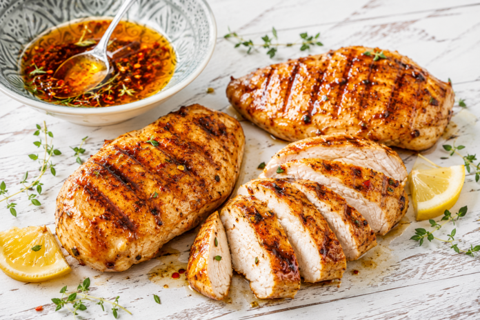 haehnchen-marinade Gegrillte Hähnchenbrust mit Hähnchen Marinade auf hellem Holztisch angerichtet.